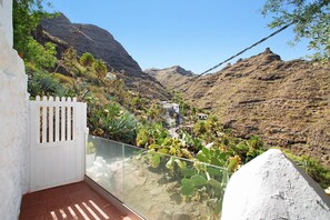 Ein Balkon mit Blick auf eine gebirgige Landschaft, einem weißen Tor und einem Glasgeländer.
