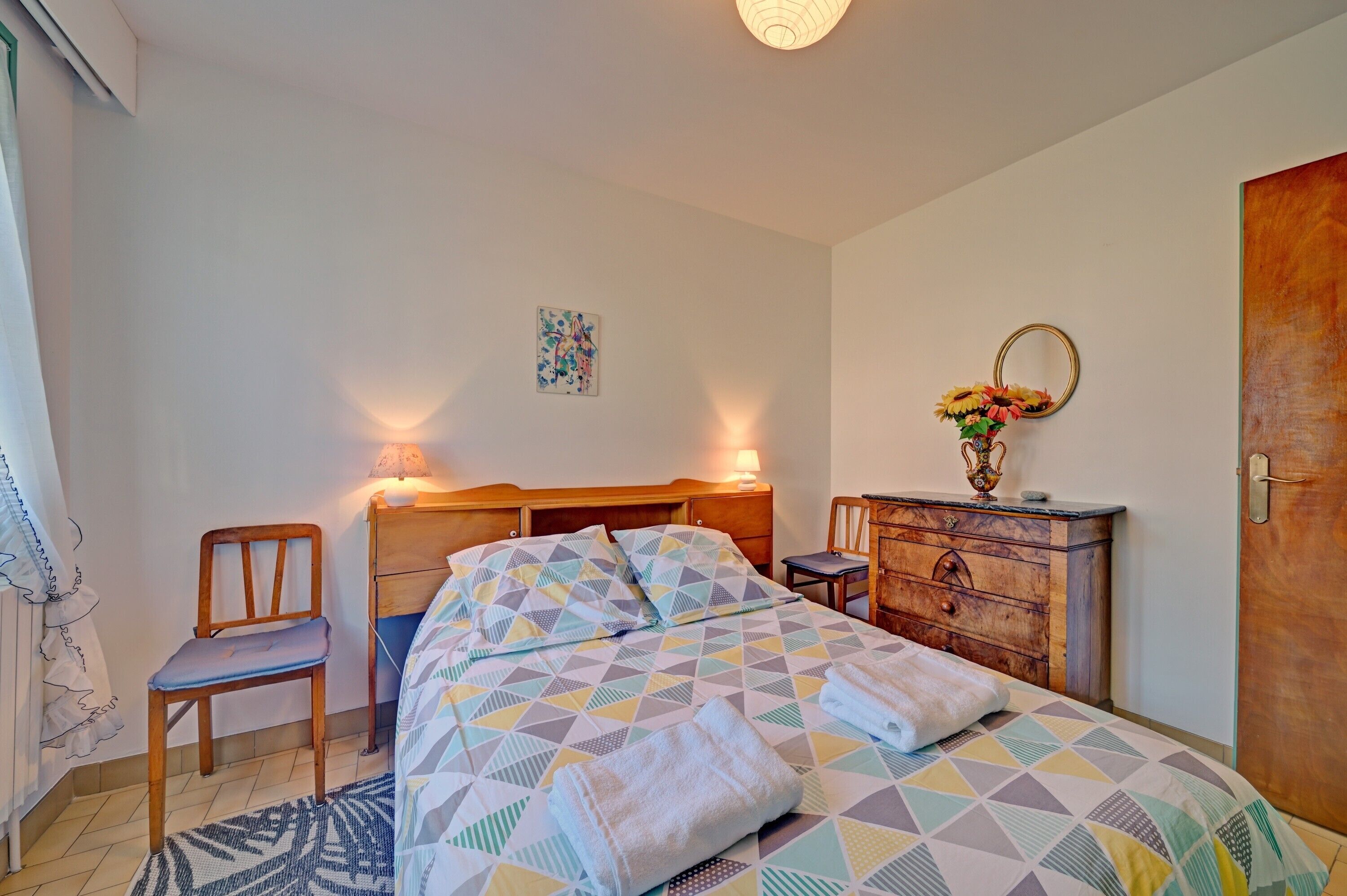 Une chambre à coucher comprenant un lit, une chaise, une commode, un miroir et un tableau accroché au mur.