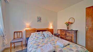 Une chambre à coucher comprenant un lit, une chaise, une commode, un miroir et un tableau accroché au mur.