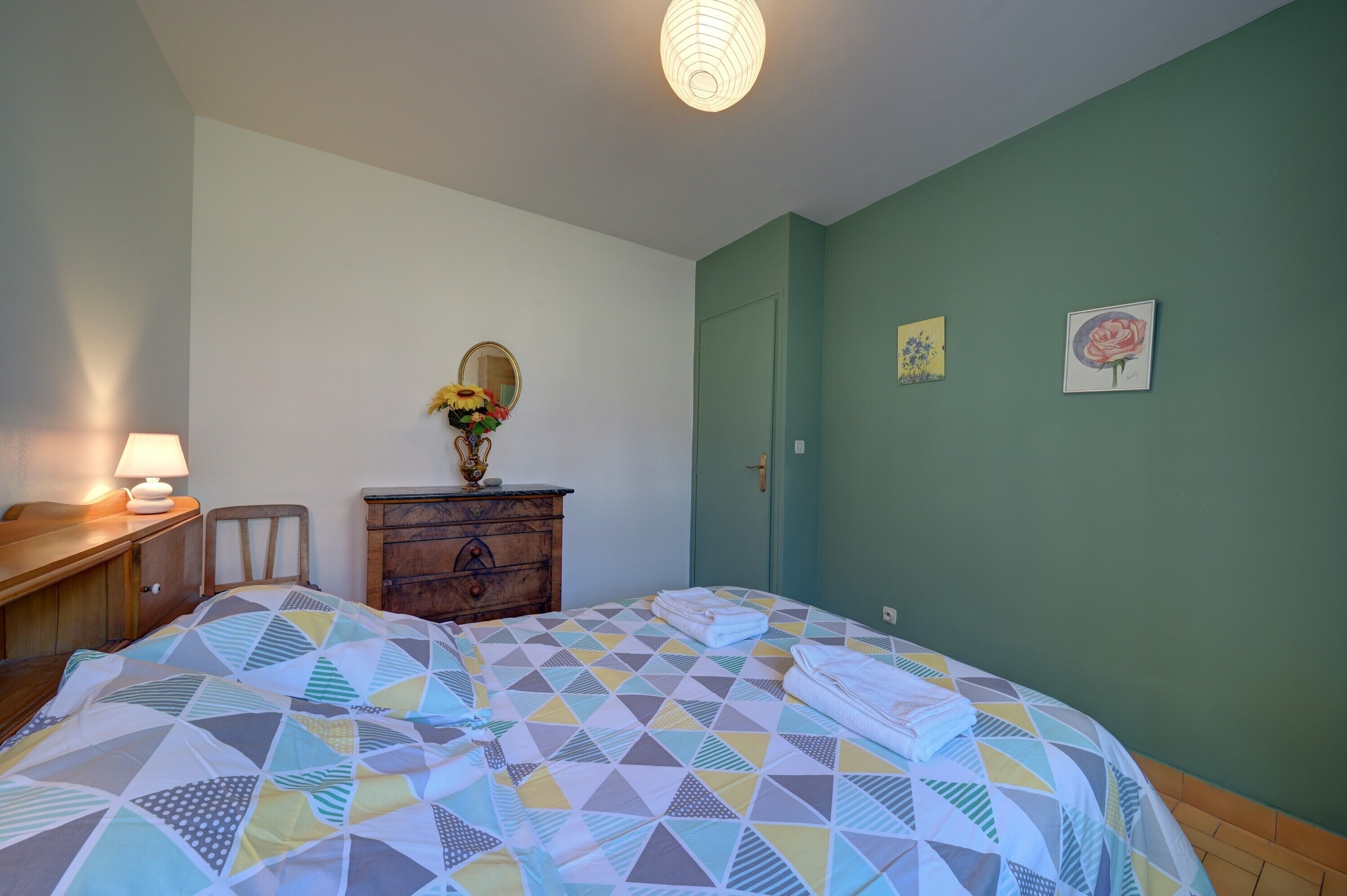 Un dormitorio con una colcha de estampado geométrico, un aparador de madera, un espejo y una lámpara de pared.