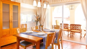 Un coin repas avec une table en bois dressée pour quatre personnes, des chaises, un buffet et une vue à travers une porte vitrée.