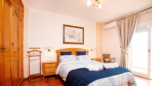 Une chambre à coucher avec un lit, une armoire en bois, une table de chevet, une chaise et une fenêtre avec des rideaux.