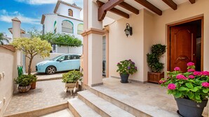 Un bâtiment avec un escalier en bois menant à une porte, des plantes en pot et une voiture garée.