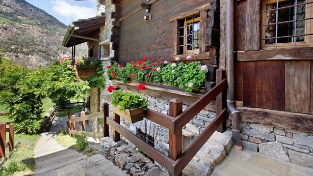 A wooden cabin with a stone foundation, wooden balcony with flower boxes, and a stone staircase leading to the entrance. - Chalet "1175" – Perfect for Groups of 6 to 9 Guests (Arvier AO)