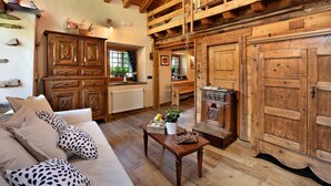 A rustic interior with a wooden ceiling, a sofa with patterned cushions, a wooden table with a basket, and a large wooden door. - Chalet "1175" – Perfect for Groups of 6 to 9 Guests (Arvier AO)