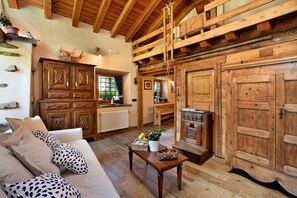 Un intérieur rustique avec un plafond en bois, un canapé agrémenté de coussins à motifs, une table en bois avec un panier, et une grande porte en bois.