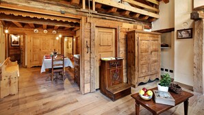 A rustic wooden interior with a dining area, wooden cabinets, and a small table with fruits and a book. - Chalet "1175" – Perfect for Groups of 6 to 9 Guests (Arvier AO)