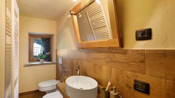 A bathroom with a wooden vanity, a round sink, a toilet, a window with a view, and a mirror.