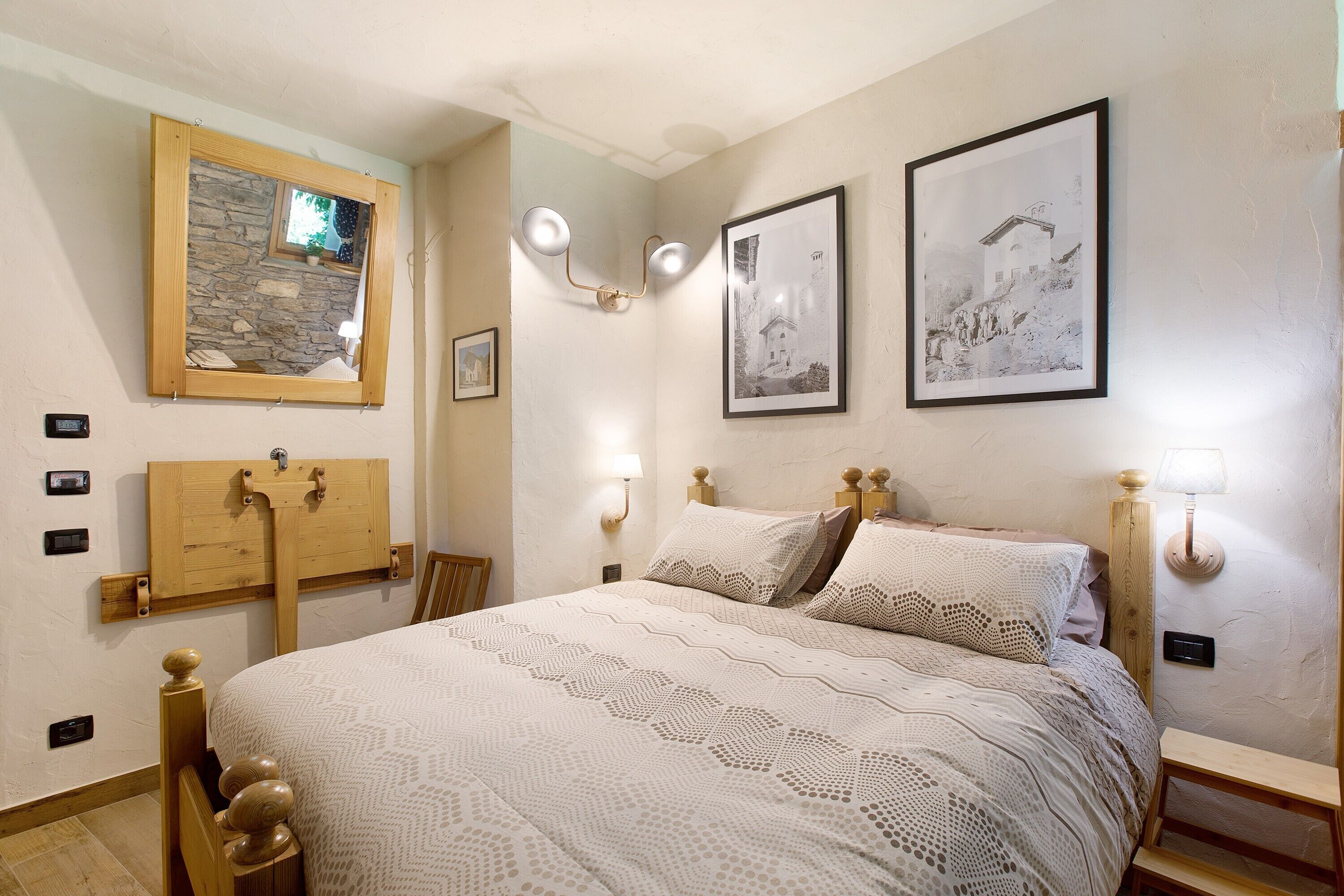 Un dormitorio con cama, cabecera de madera, luces fijadas a la pared, cuadros enmarcados y una pared de piedra decorativa.