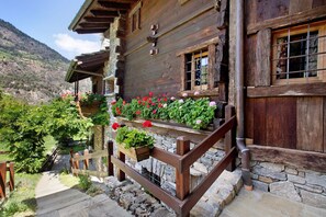 Una cabaña de madera con base de piedra, un balcón de madera con jardineras de flores y una escalera de piedra que conduce a la entrada.
