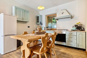 A kitchen with a wooden table, chairs, a refrigerator, a stove, and cabinets. - Chalet 'Baita Cisina' with Mountain View, Private Terrace and Wi-Fi (Villa Rendena)
