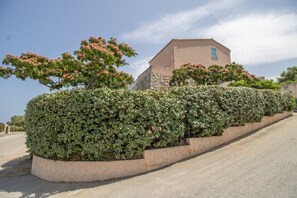 Un bâtiment à la façade en pierre, doté d’une fenêtre, et entouré de haies soigneusement taillées et d’arbres en fleurs.