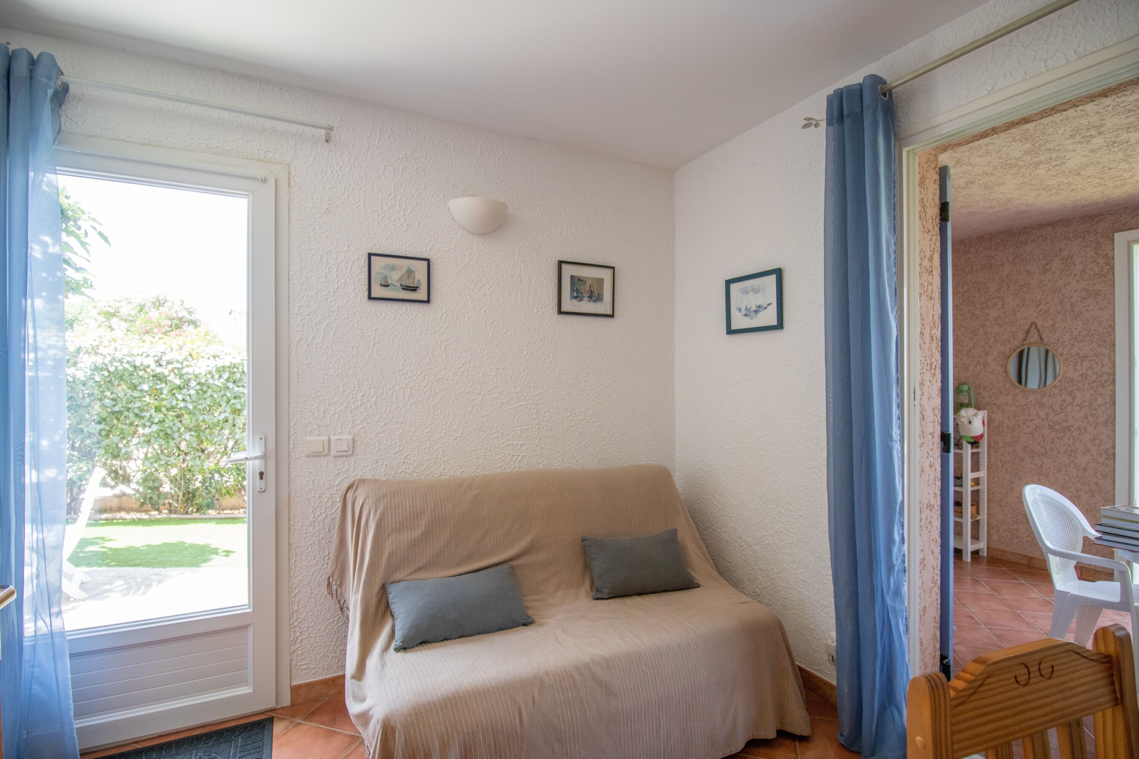 Une pièce comprenant un canapé, deux coussins, une porte donnant sur l’extérieur et un mur orné de trois tableaux encadrés.