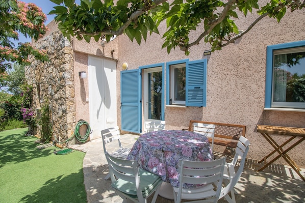 Une terrasse avec une table ronde et des chaises, un petit jardin et un mur en pierre.