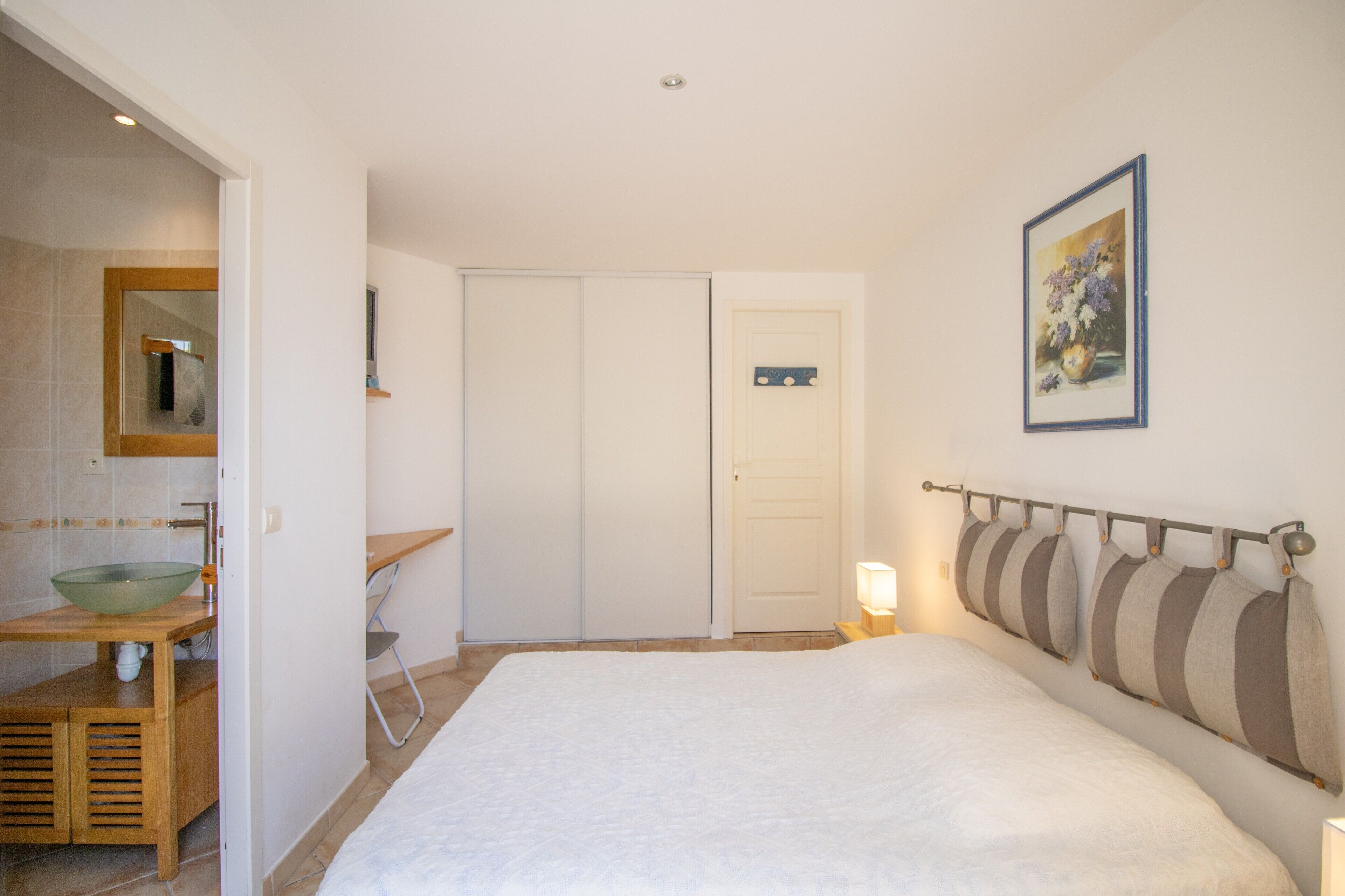 Ein Schlafzimmer mit einem Bett, einem Nachttisch, einem Spiegel, einem Waschbecken und einer Tür.