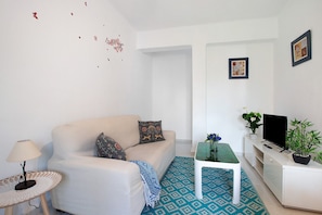 A living room with a sofa, a coffee table, a TV, and a small table with a lamp.