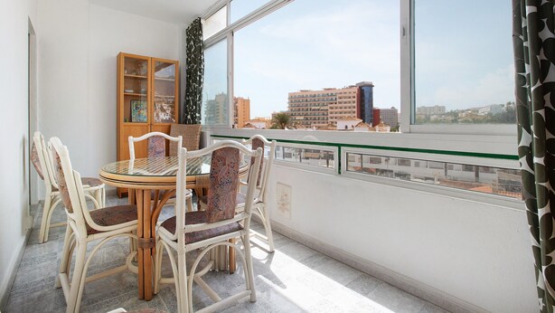 A balcony with a dining table and chairs, a glass cabinet, and a view of buildings across a body of water. - Apartment 'Prealsa Benalmádena' with Sea View, Shared Pool and Private Terrace (Benalmádena)