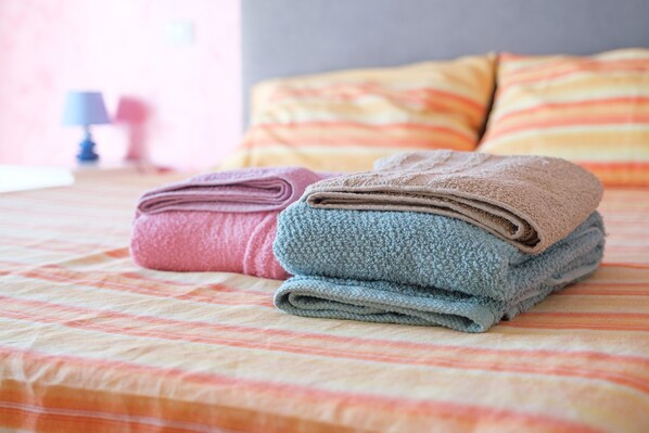 A neatly made bed with folded towels in pink and blue.