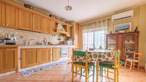 A kitchen with wooden cabinets, a dining table with chairs, a tiled floor, and an air conditioning unit. - Apartment 'Meizon Sicilia' with Balcony, Wi-Fi and Air Conditioning (terme vigliatore)