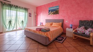 A bedroom with a bed, a chair, a nightstand, a lamp, a picture on the wall, and a window with curtains. - Apartment 'Meizon Sicilia' with Balcony, Wi-Fi and Air Conditioning (terme vigliatore)