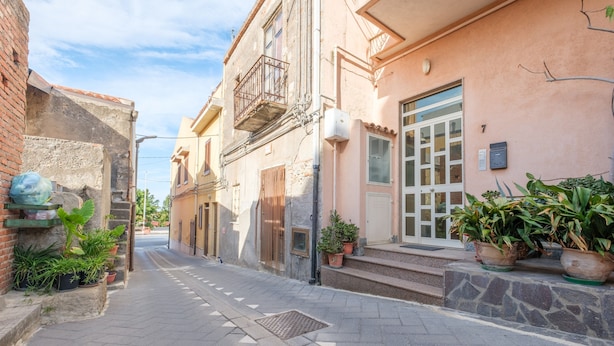 A narrow street with buildings on either side, potted plants, and a clear sky. - Apartment 'Meizon Sicilia' with Balcony, Wi-Fi and Air Conditioning (terme vigliatore)