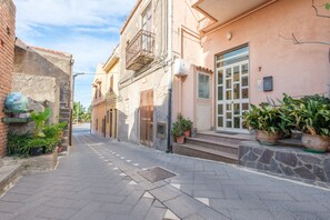 Une rue étroite, bordée de bâtiments des deux côtés, avec des plantes en pot et un ciel dégagé.