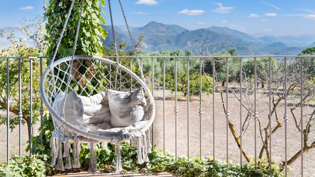 A white hanging chair with cushions, a metal fence, and a view of mountains in the background.