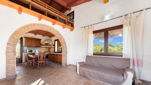 A cozy living area with a sofa, a dining table with chairs, an archway leading to a kitchen, and a window with curtains.