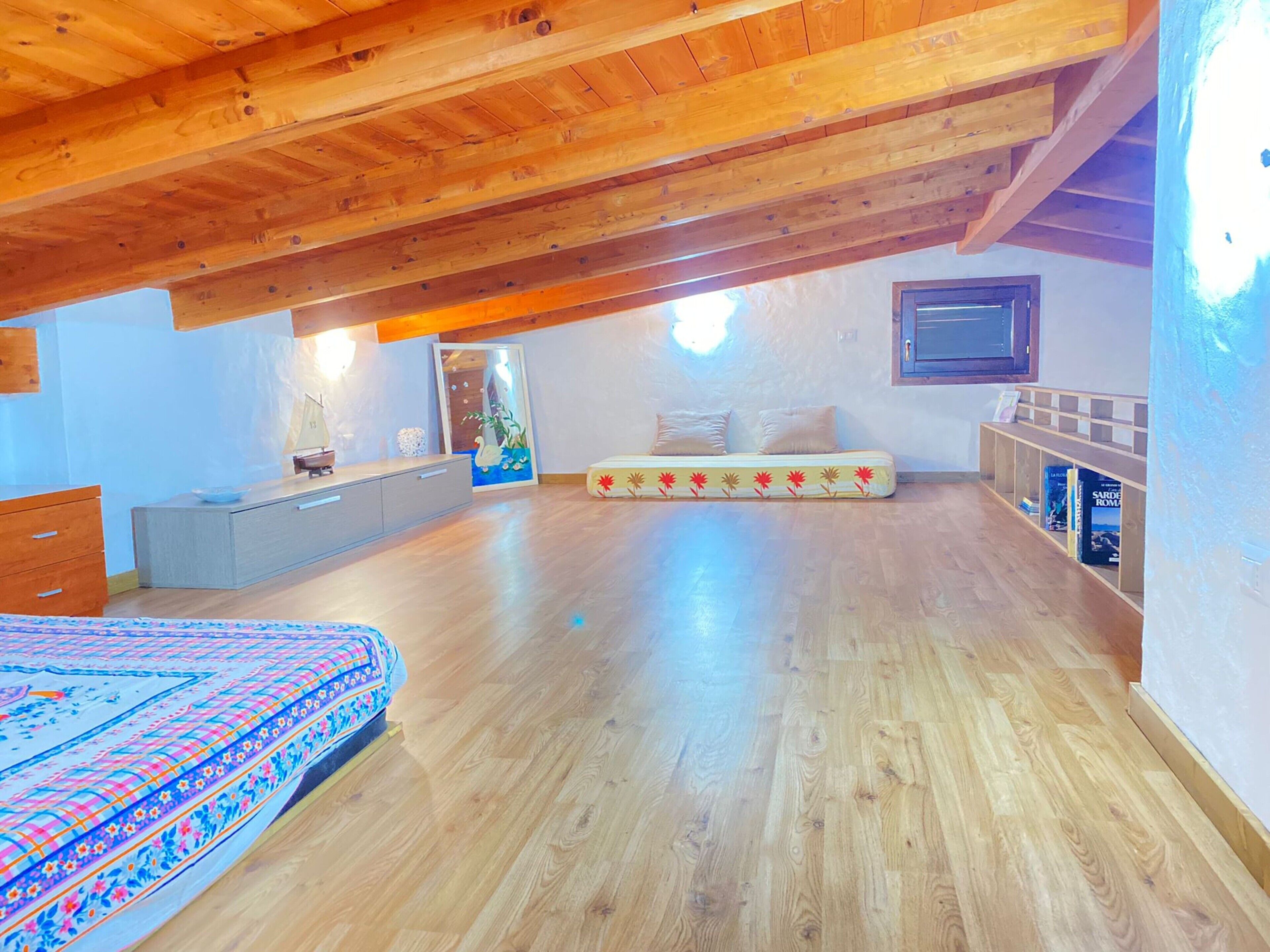 Une chambre spacieuse située dans les combles, avec un plafond en bois, un lit, un canapé et un petit espace bureau.
