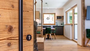 A modern interior with a wooden door, a dining area with chairs, a kitchen, and large windows. - Holiday Apartment "Chalet Kasch Glück" with Mountain View, Private Terrace & Wi-Fi (Fiè allo Sciliar)