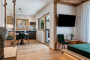 Una habitación moderna con suelo de madera, cama, televisor, zona de comedor y vistas al exterior.