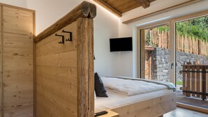 Una cama de madera con televisión integrada, una pared de piedra al exterior y una puerta de madera.