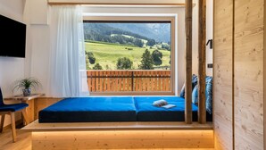 Una habitación con un ventanal grande, un banco de madera, un televisor y una planta.