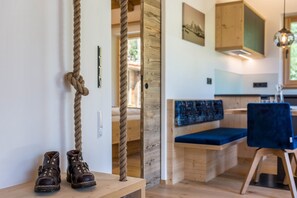 Un banc en bois avec un coussin bleu, une paire de bottes marron posée sur une étagère en bois, et une corde suspendue au mur.