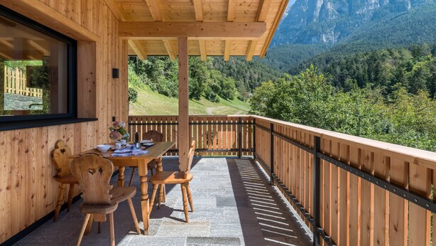 Terraza de madera con mesa y sillas, con vistas a un paisaje montañoso.
