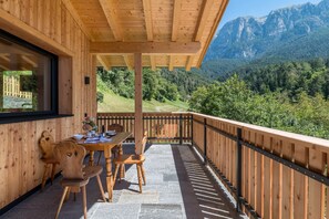 Terraza de madera con mesa y sillas, con vistas a un paisaje montañoso.