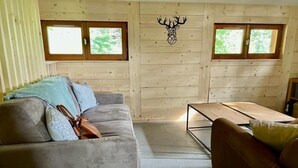 Une pièce chaleureuse avec un canapé gris, un divan en cuir marron et un mur en bois doté de deux fenêtres.