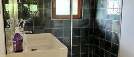 Een badkamer met een wastafel, spiegel, raam en douchehoek.