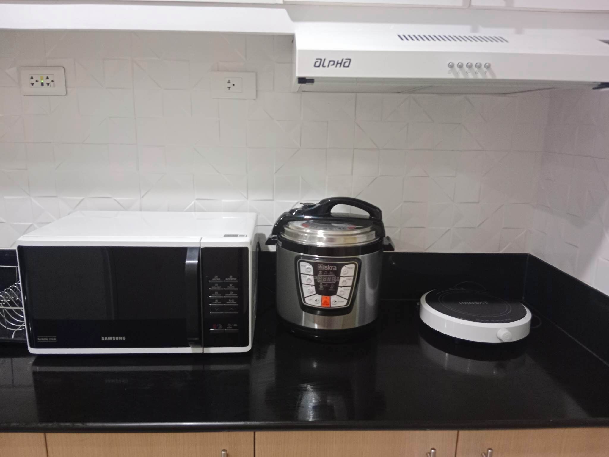 A kitchen with a microwave, a slow cooker, and a rice cooker on a black countertop.