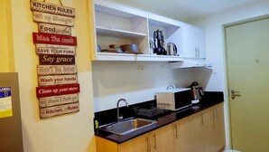 Une cuisine compacte avec des meubles hauts blancs, un plan de travail noir et un évier en acier inoxydable. Un panneau indiquant les règles à respecter dans la cuisine est visible sur le mur.