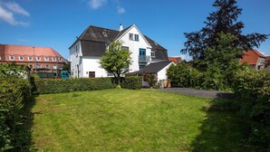 A residential property with a well-maintained lawn, a large house with a dark roof, and a neighboring building with a red roof. - Spacious 2-Bed Apartment in Aalborg (Aalborg)
