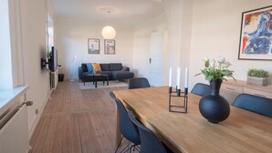 A modern living room with a wooden dining table, black chairs, a black vase with white flowers, a black sofa, and a white radiator. - Spacious 2-Bed Apartment in Aalborg (Aalborg)