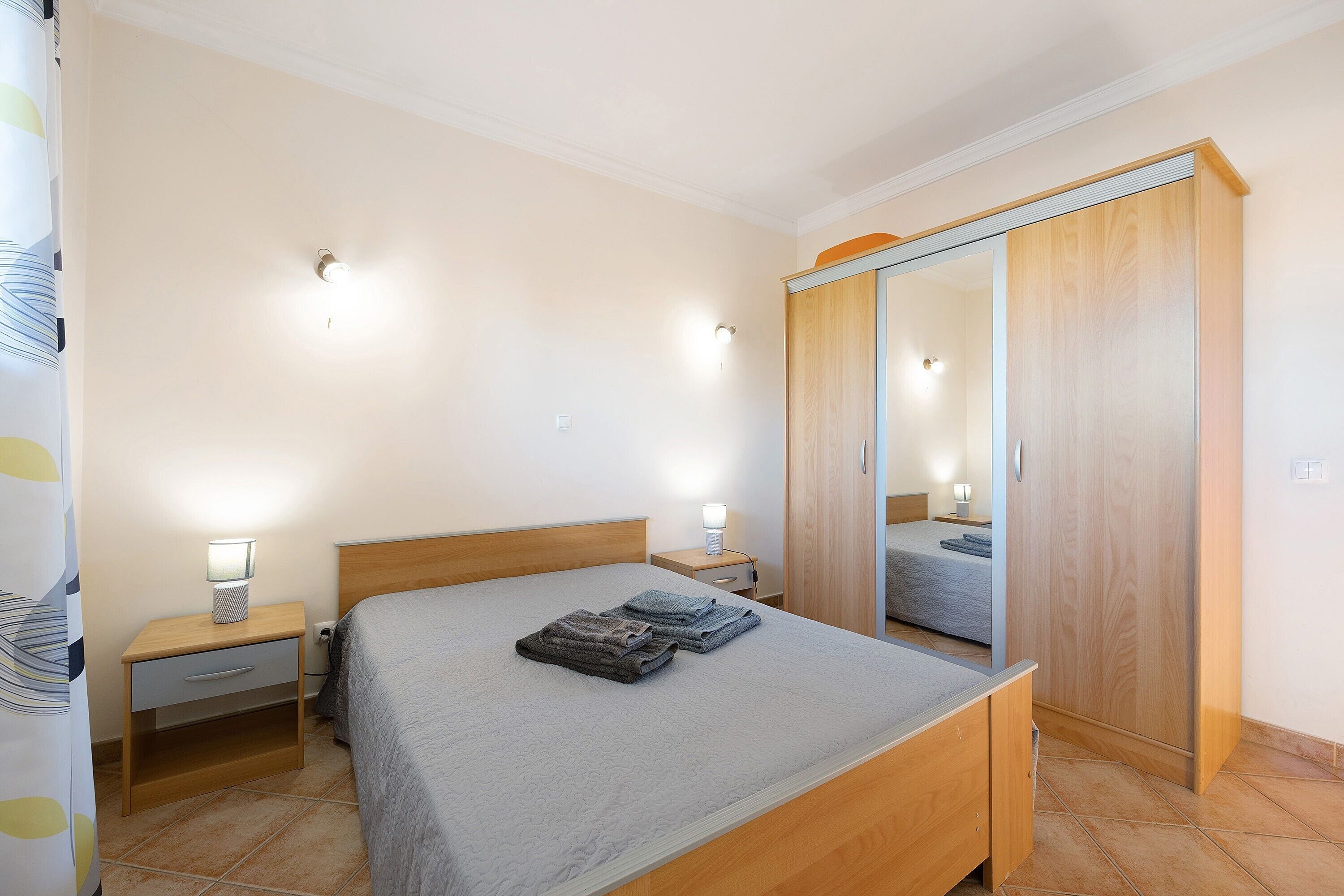 A bedroom with a bed, nightstands, a wardrobe, and a mirror.
