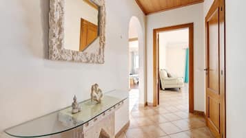 A hallway with a glass-top console table, a decorative mirror, and a statue.