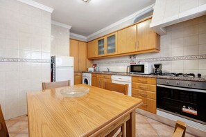 Une cuisine dotée de meubles en bois, d’un four à micro-ondes, d’une cuisinière, d’un lave-vaisselle et d’une table à manger avec des chaises.