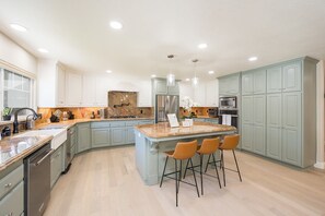 A modern kitchen with a central island, bar stools, and stainless steel appliances. - 4,500 sq-ft retreat with a pool and hot tub in the middle of wine country!  (Templeton)