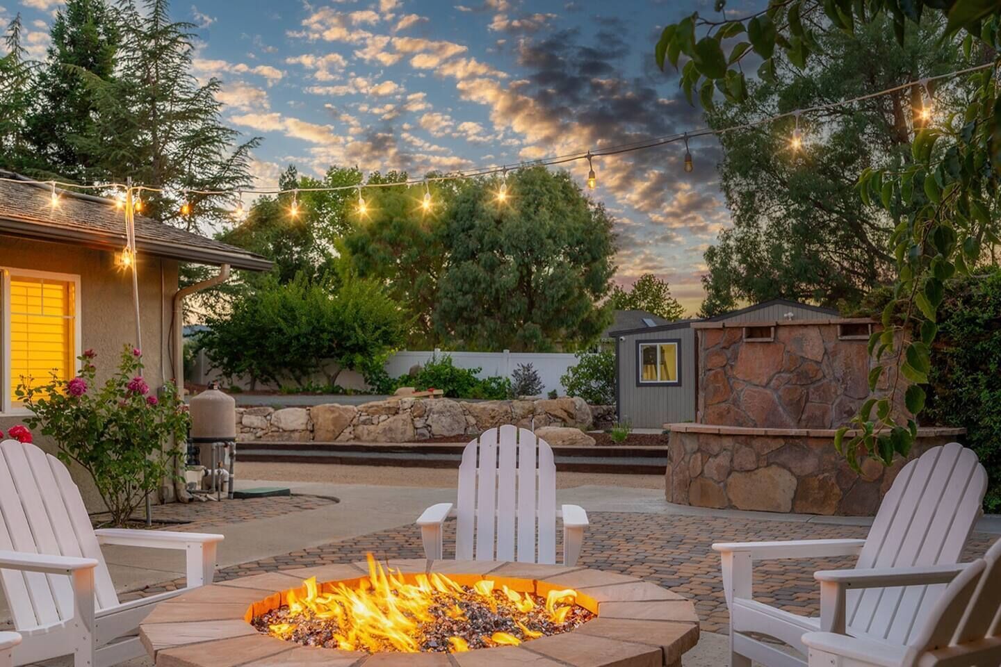 Un espace patio avec un foyer, des fauteuils Adirondack blancs et des guirlandes lumineuses.