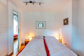 A bedroom with a bed, bedside lamps, a framed picture on the wall, and a door leading to another room.