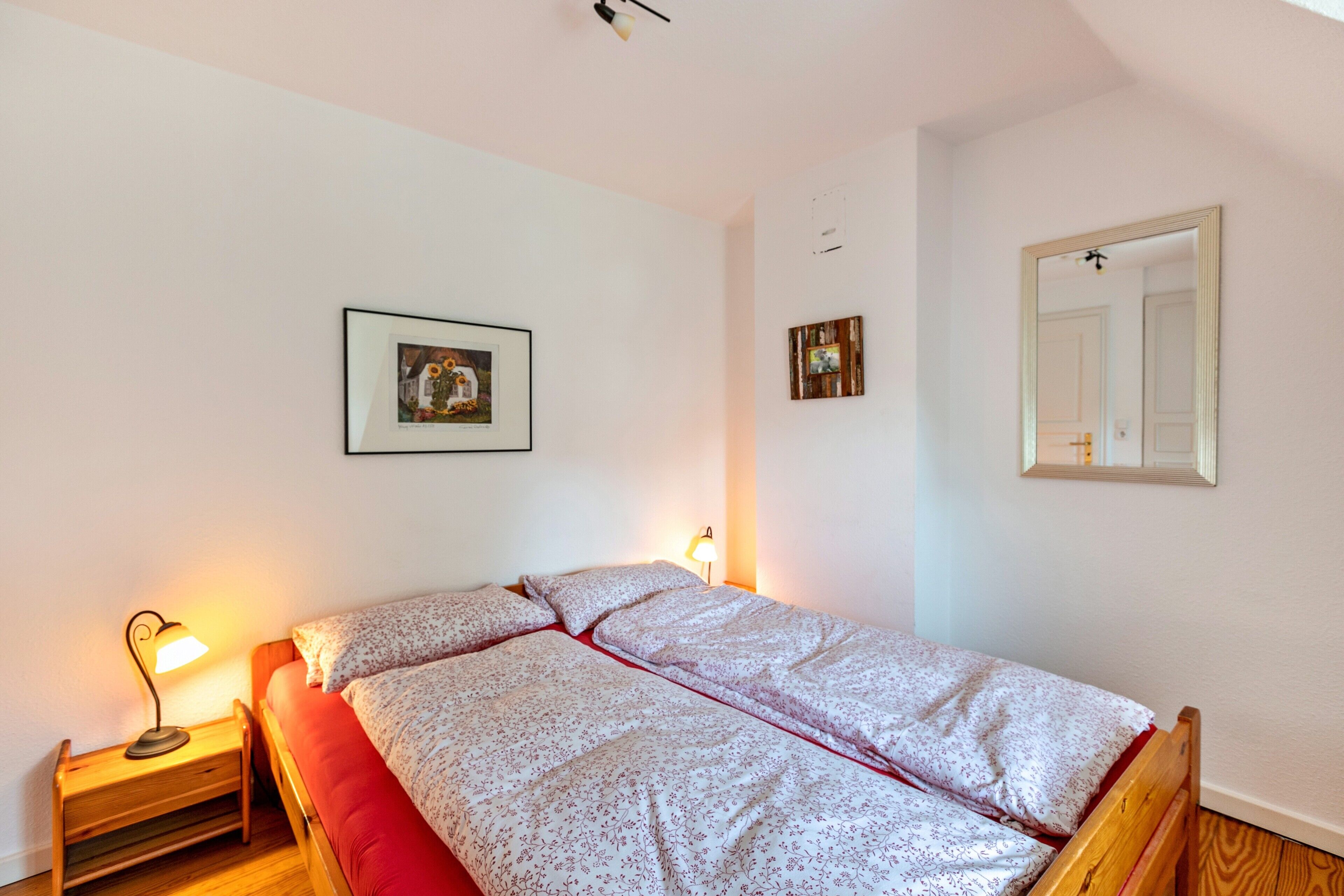 Une chambre à coucher avec un lit, deux lampes de chevet, un tableau encadré et un miroir au mur.