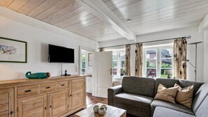 Una sala de estar con un aparador de madera, un sofá gris, una mesita de madera y un televisor montado en la pared.